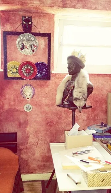 Inside a shared studio space, artists work on diverse projects: painting, sculpture, and digital art. Tools and materials are visible, creating a sense of organized chaos and creative energy.