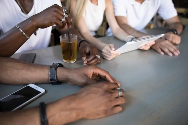 A close-up shot of a diverse group of people gathered around a table at a community event, with laptops and smartphones visible. The setting is a local coffee shop or community center, symbolizing the grassroots nature of alternative media and citizen journalism.