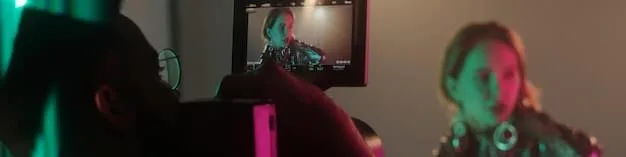 A behind-the-scenes shot of a small, energetic music video set. The image shows a group of friends working together, some holding lights, others adjusting the camera, and the artist performing. The setting is a cozy, creatively decorated room.