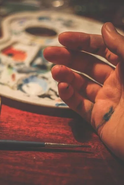 A close-up shot of an artist's hands meticulously crafting a piece of alternative art in their studio, surrounded by various art supplies and tools. The scene captures the dedication and passion behind the creation process.