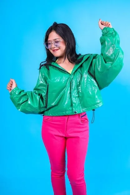 A person wearing a bright red PVC skirt paired with a neon green graphic t-shirt and chunky platform boots. They are accessorized with multiple silver chain necklaces and colorful hair clips. The background is a vibrant, graffiti-covered alleyway.