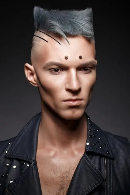 A close-up shot of a young man's face, adorned with intricate facial piercings and dark eyeliner. He is wearing a high-collared, studded leather jacket and has a confident, direct gaze.