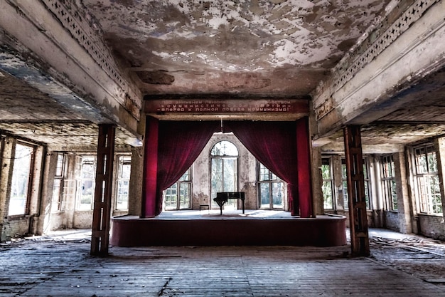 Inside an abandoned theater in Gary, Indiana. The ornate plasterwork on the walls and ceiling is crumbling, but still shows glimpses of its former grandeur. Rows of decaying seats stretch into the darkness, suggesting the echoes of past performances.