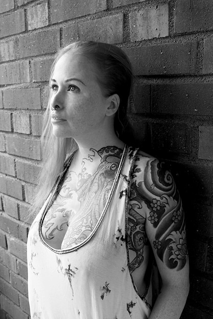 A black and white photograph of a heavily tattooed individual from the 1950s, showcasing traditional sailor tattoos and a rebellious attitude, capturing the historical context of body modification in American subculture.