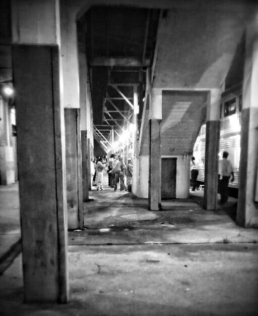 A black and white photograph of an abandoned industrial site, with a group of people conducting a ritualistic performance art piece. They are wearing masks made of recycled materials and interacting with the decaying machinery, symbolizing the confrontation with industrial decay and the attempt to reclaim a connection to nature through artistic expression.