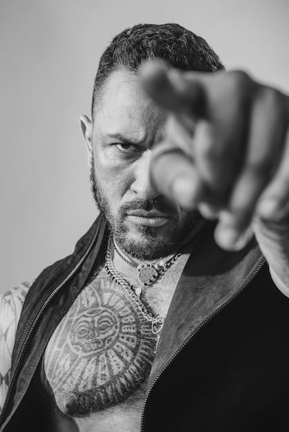 A black and white portrait of a heavily tattooed individual from the early 20th century, showcasing traditional tattoo designs and a confident, unconventional presence.