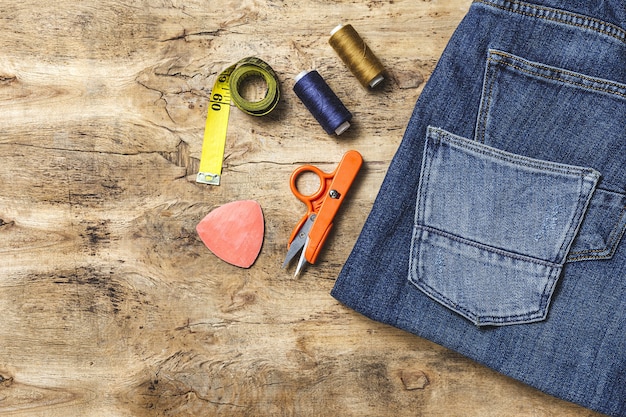 A flat lay featuring various DIY tools and materials for deconstructing denim, including scissors, seam rippers, patches of different denim washes, and sewing supplies. The arrangement suggests creativity and customization.