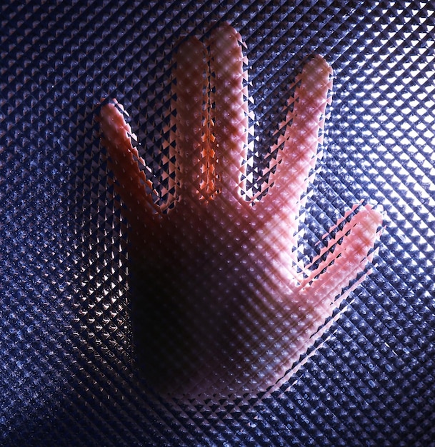 A close-up of a hand holding a small sample of 3D-printed fabric with a unique, flexible texture. The fabric is made of a translucent material, and the background is a blurred workshop setting.