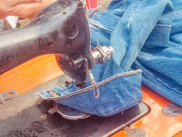 Close-up of hands using a sewing machine to repurpose a vintage denim jacket with colorful patches and embroidery, illustrating sustainable and budget-friendly material sourcing for an underground fashion brand.