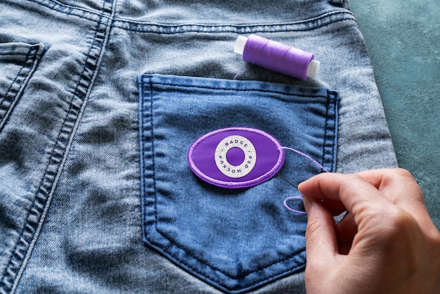 A close-up shot of a hand meticulously sewing a patch onto a denim jacket, showcasing the DIY and personalized aspect of underground fashion.