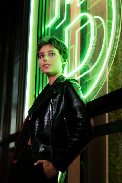 A close-up shot of a person wearing a neon green vinyl jacket with black mesh detailing. The jacket is paired with a bright pink beanie and chunky silver jewelry. The background is blurred, highlighting the vibrant colors and textures of the outfit.