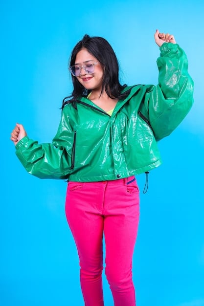 A person wearing a bright red PVC skirt paired with a neon green graphic t-shirt and chunky platform boots. They are accessorized with multiple silver chain necklaces and colorful hair clips. The background is a vibrant, graffiti-covered alleyway.