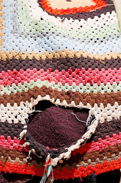 A detailed close-up shows a hand-stitched garment featuring asymmetrical patterns and a mix of recycled materials. The lighting highlights the intricate craftsmanship and the raw textures of the fabric, emphasizing the garment's unique, handcrafted nature.