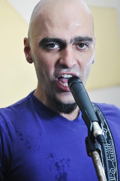 A close-up, dynamic shot of a lead singer from an alternative band, mid-performance, with sweat on their brow and intense vocal expression. The background is blurred stage lights, creating motion and energy.
