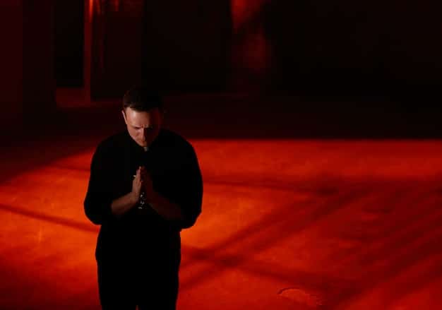 A small, minimalist stage bathed in warm, dramatic lighting, with a single actor performing a monologue. The focus is on the emotional intensity and effectiveness of simple staging.