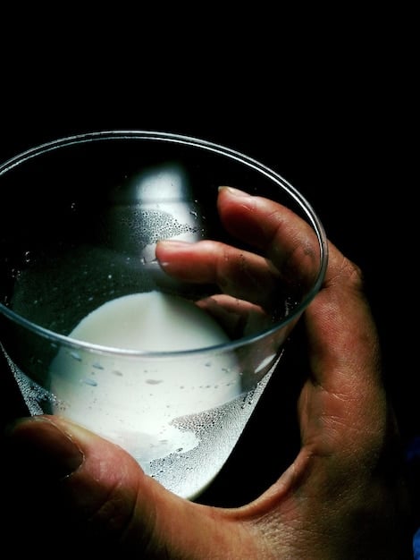 A close-up of a wet plate collodion photographer's hands carefully pouring chemicals onto a glass plate in a dimly lit studio, intricate details visible.