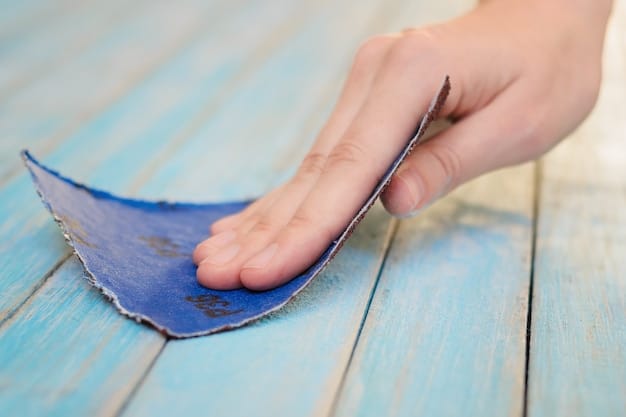 A close-up of a pair of blue jeans being distressed with sandpaper, showing faint white marks and fibers starting to emerge, on a wooden surface.