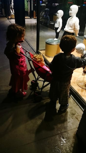 A bustling scene inside an underground fashion trade show, with diverse attendees examining unique, handcrafted garments on display. The lighting is moody, reflecting an independent, artistic vibe.